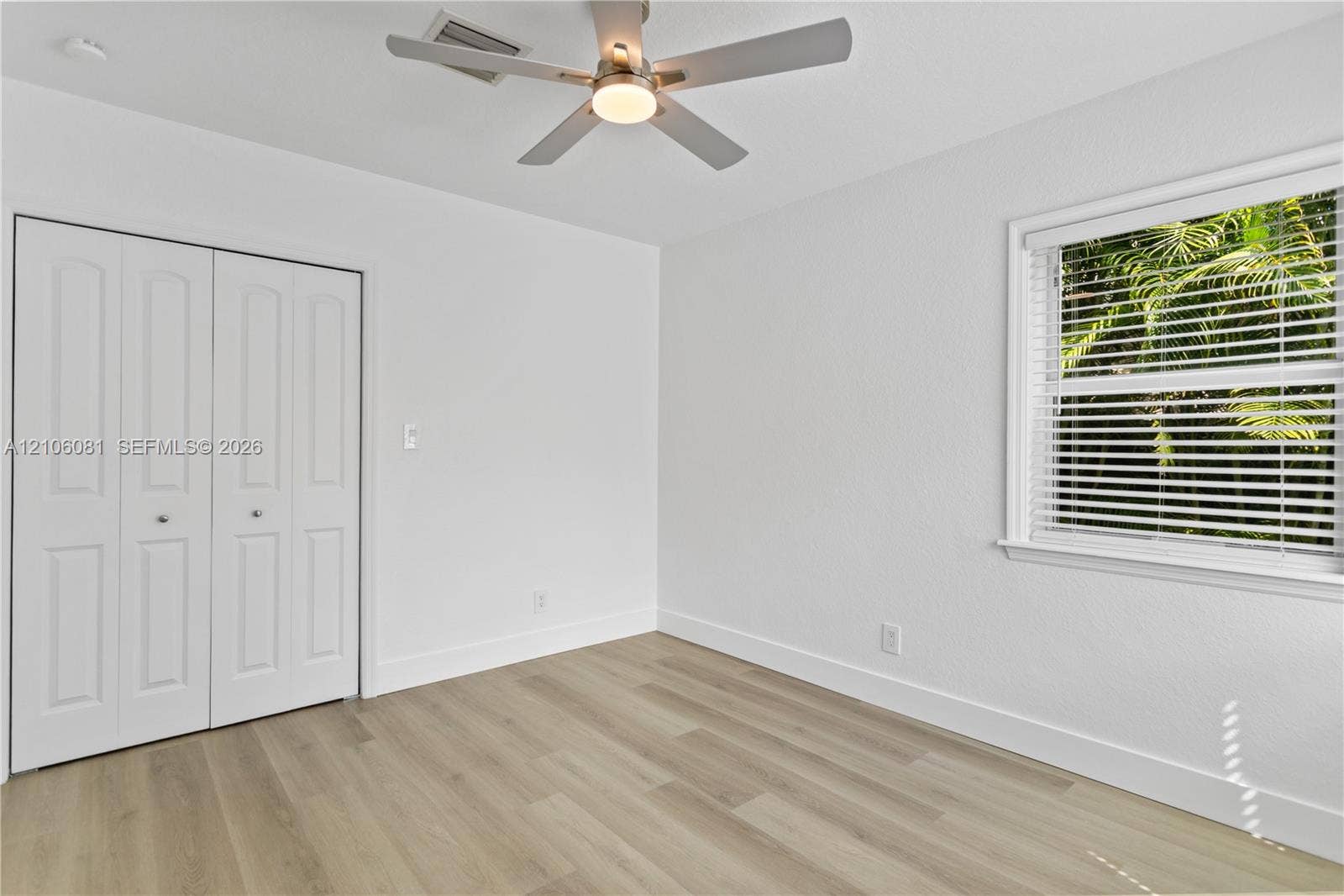 Room featuring wood-finish flooring, white walls, double-door closet, ceiling fan with integrated light, and a window with horizontal blinds
