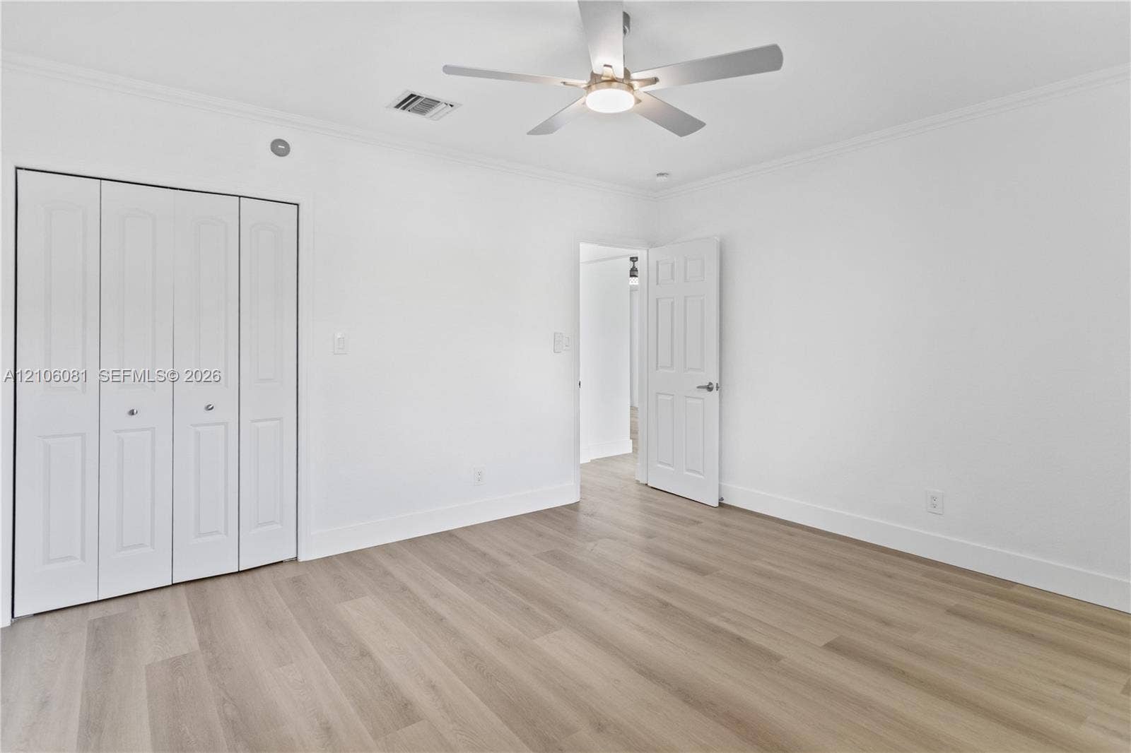 Interior space featuring wood-finish flooring, a multi-panel door, built-in bi-fold closet doors, and a ceiling fan with integrated lighting