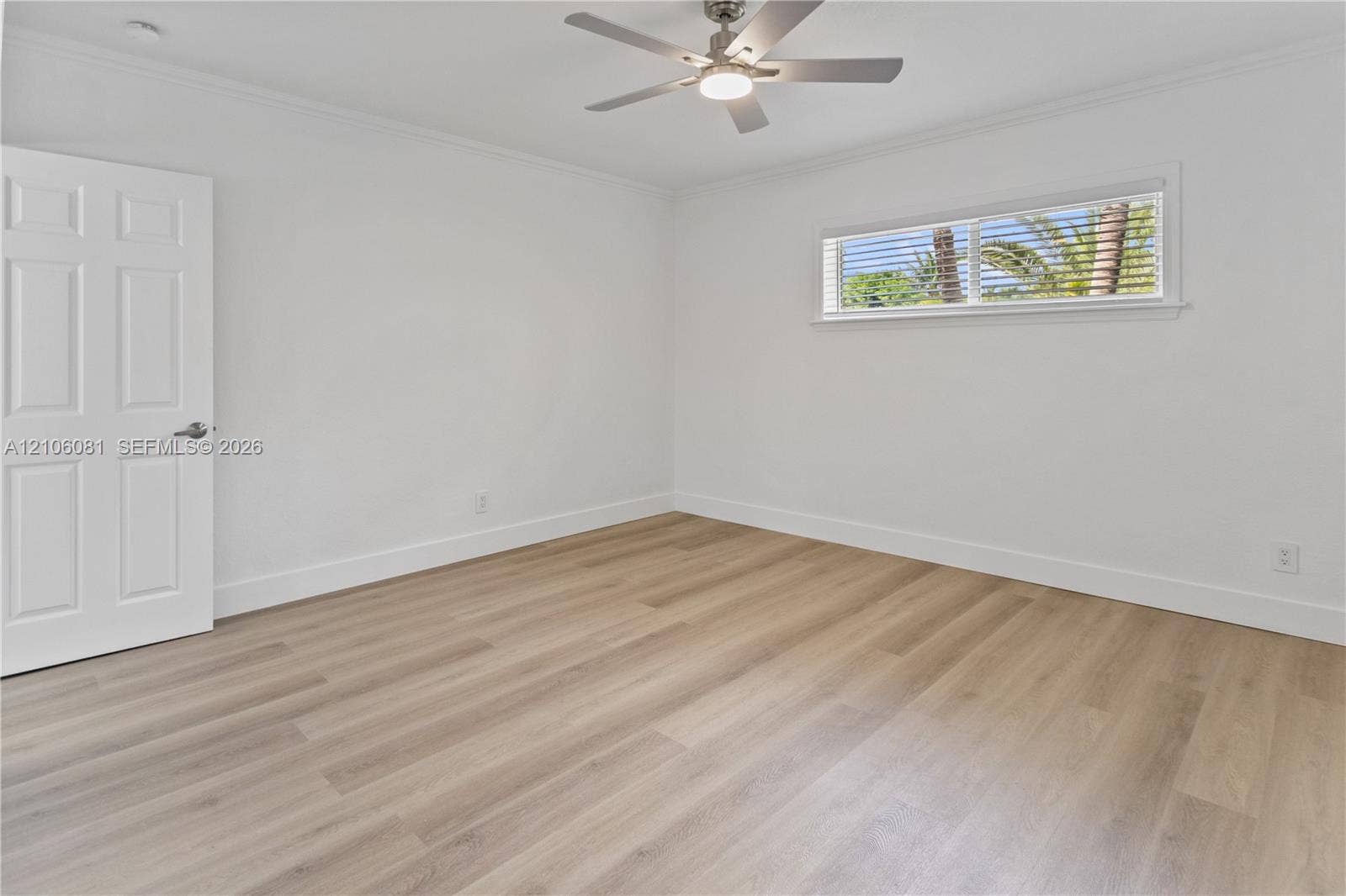 Room featuring light wood-finish flooring, a six-panel door, and a ceiling fan with integrated lighting
