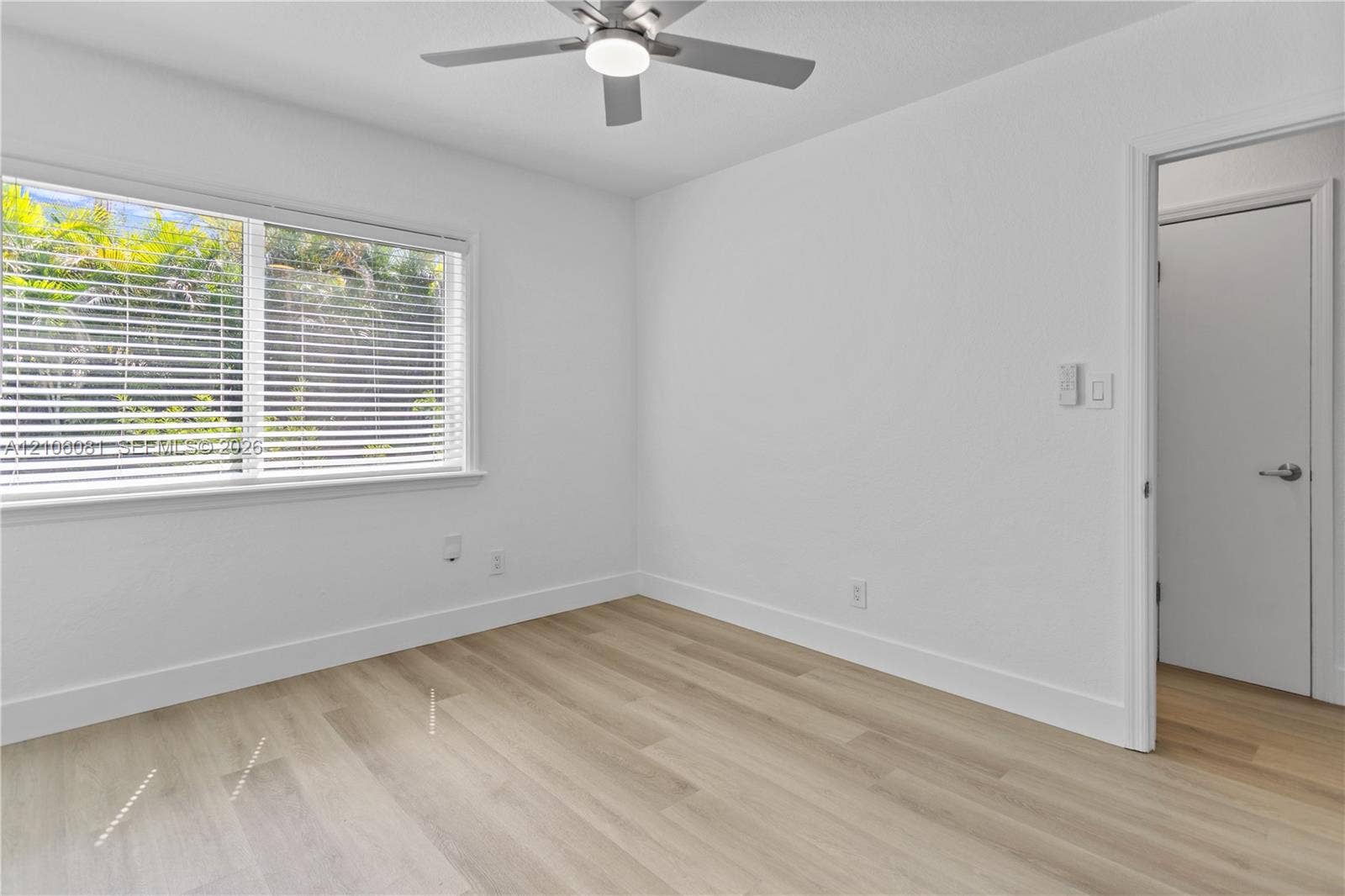 Room featuring wood-finish flooring, a neutral-toned wall finish, a multi-blade ceiling fan with an integrated light fixture, and horizontal window blinds