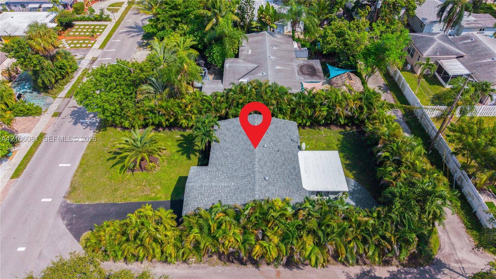 Corner lot featuring mature palm landscaping, asphalt driveway, and a covered patio area