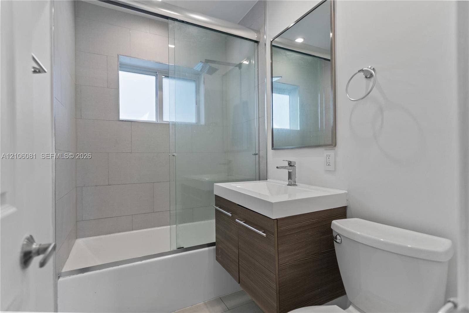 Floating vanity with wood-finish cabinetry, rectangular integrated sink, glass-enclosed shower, and large-format tile surround