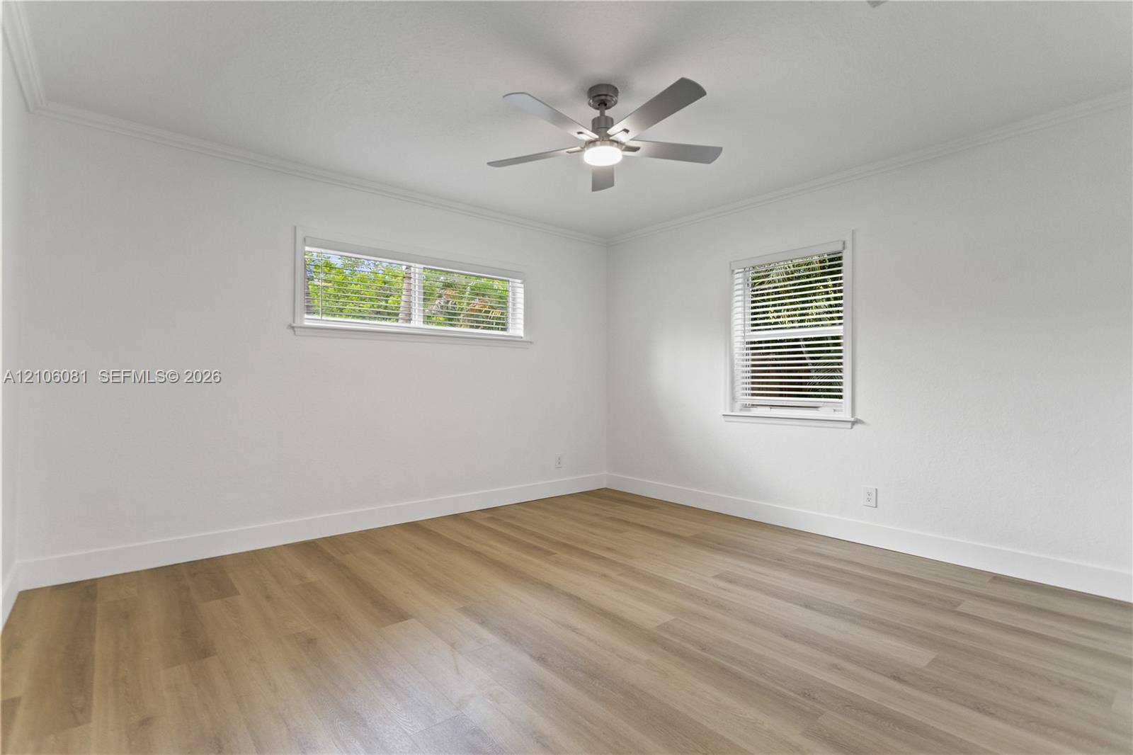 Neutral interior featuring wood-finish flooring, white walls, crown molding, multi-pane windows with horizontal blinds, and a central ceiling fan with an integrated light fixture