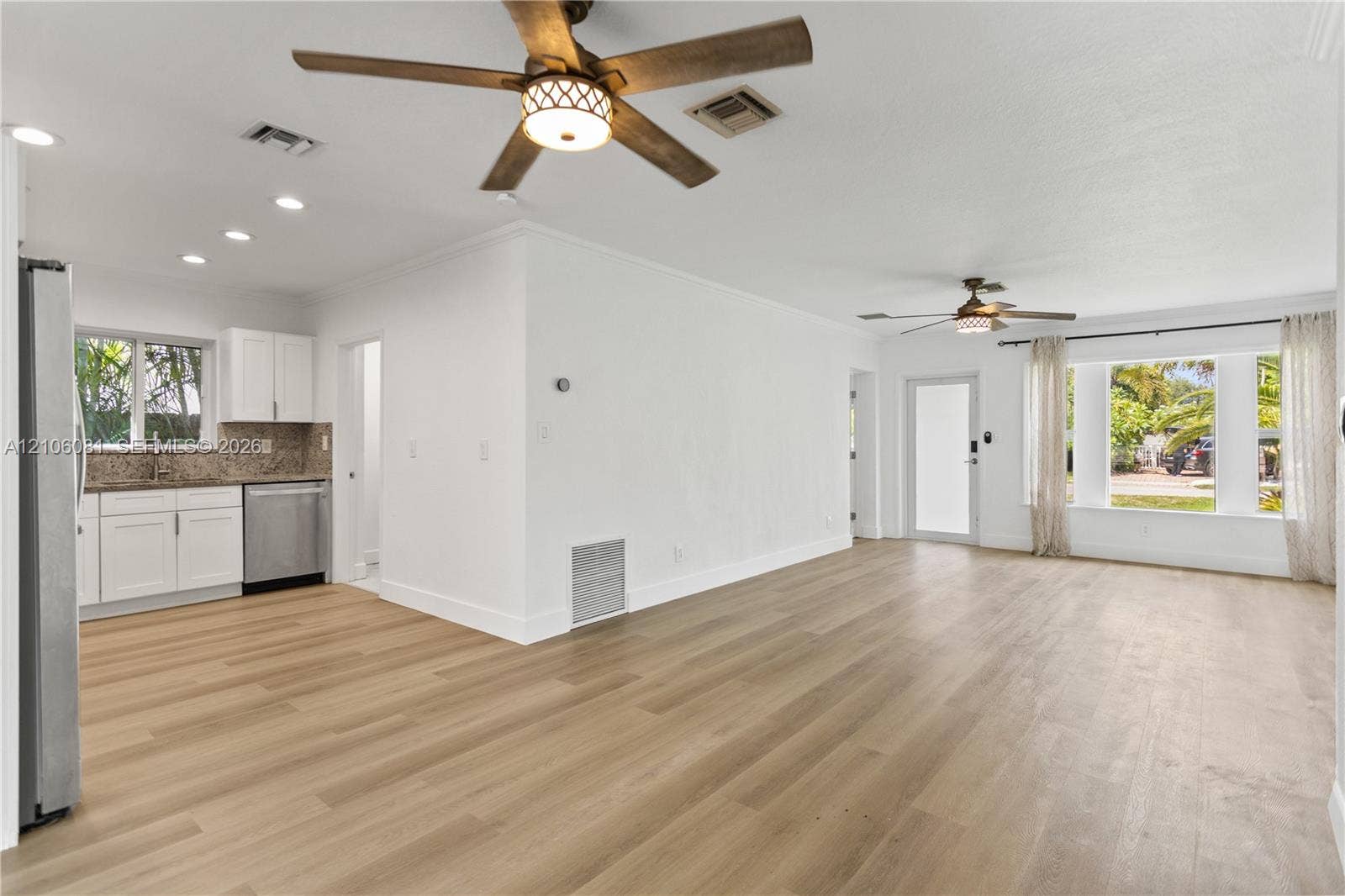 Open floor plan featuring wood-finish flooring, recessed lighting, ceiling fans, and a kitchen equipped with white cabinetry and stainless-steel appliances