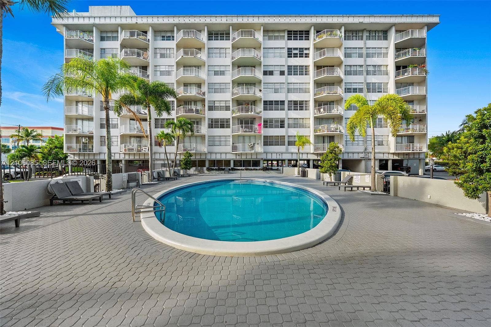 16710 NE 9th Avenue, #705, North Miami Beach, North Miami Beach, FL 33162 Oval swimming pool surrounded by a paver deck, palm landscaping, and multi-story building featuring private balconies