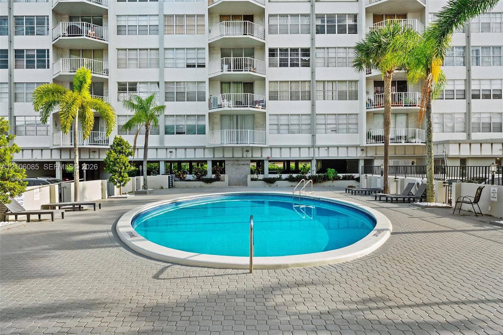 16710 NE 9th Avenue, #705, North Miami Beach, North Miami Beach, FL 33162 Circular swimming pool with a concrete pool deck, surrounding palm trees, and multi-story building facade featuring private balconies