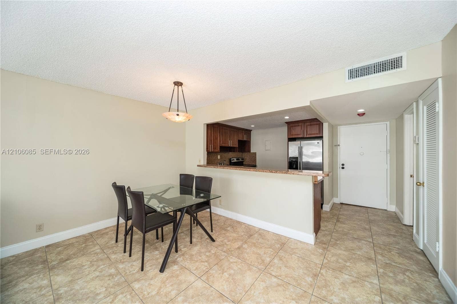 16710 NE 9th Avenue, #705, North Miami Beach, North Miami Beach, FL 33162 Dining area featuring tile flooring, a tiered pendant light fixture, and a pass-through opening to the kitchen with wood cabinetry and countertop seating