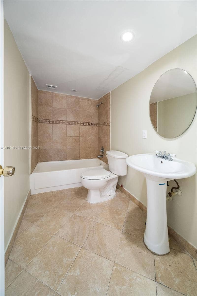 16710 NE 9th Avenue, #705, North Miami Beach, North Miami Beach, FL 33162 Full bathroom featuring neutral tile flooring, a pedestal sink, a circular wall-mounted mirror, and a bathtub with tile surround