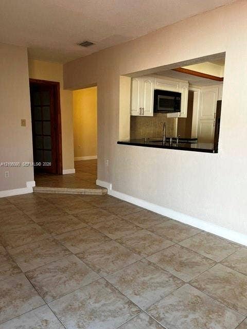 1325 N 74th Terrace, #0, Hollywood, Hollywood, FL 33024 Ceramic tile flooring, kitchen pass-through window with dark countertop, white shaker-style cabinetry, and glass-paneled interior door