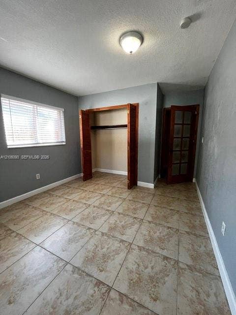1325 N 74th Terrace, #0, Hollywood, Hollywood, FL 33024 Room featuring large-format stone-patterned tile flooring, multi-pane wood door, closet with louvered wood-finish bifold doors, and window with horizontal blinds