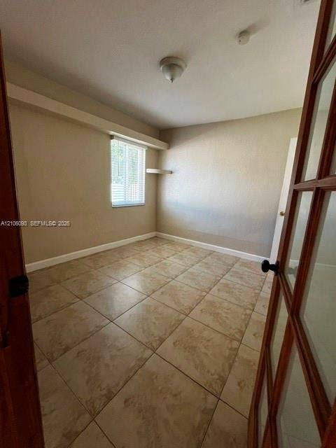 1325 N 74th Terrace, #0, Hollywood, Hollywood, FL 33024 Interior room featuring large-format ceramic tile flooring, a window with horizontal blinds, built-in corner shelving, and a wood-framed glass-paneled entry door