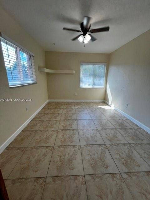 1325 N 74th Terrace, #0, Hollywood, Hollywood, FL 33024 Neutral-toned interior space featuring ceramic tile flooring, a mounted ceiling fan with integrated lighting, two windows with horizontal blinds, and a built-in corner shelf