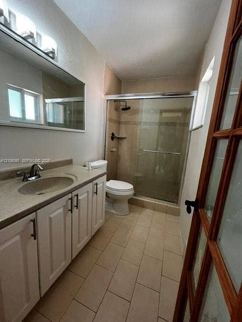 1325 N 74th Terrace, #0, Hollywood, Hollywood, FL 33024 White cabinetry with dark hardware, stone-composite countertop, full-width vanity mirror, tile flooring, and walk-in shower with a sliding glass enclosure