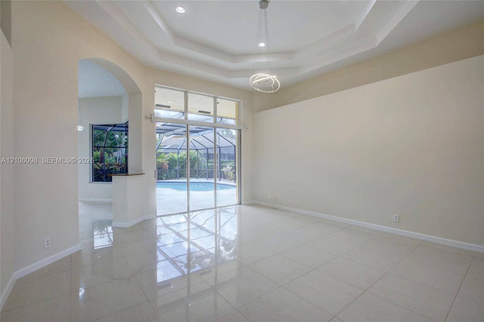 Interior space featuring tile flooring, a recessed tray ceiling, architectural archway, and expansive sliding glass doors opening to a screened pool enclosure
