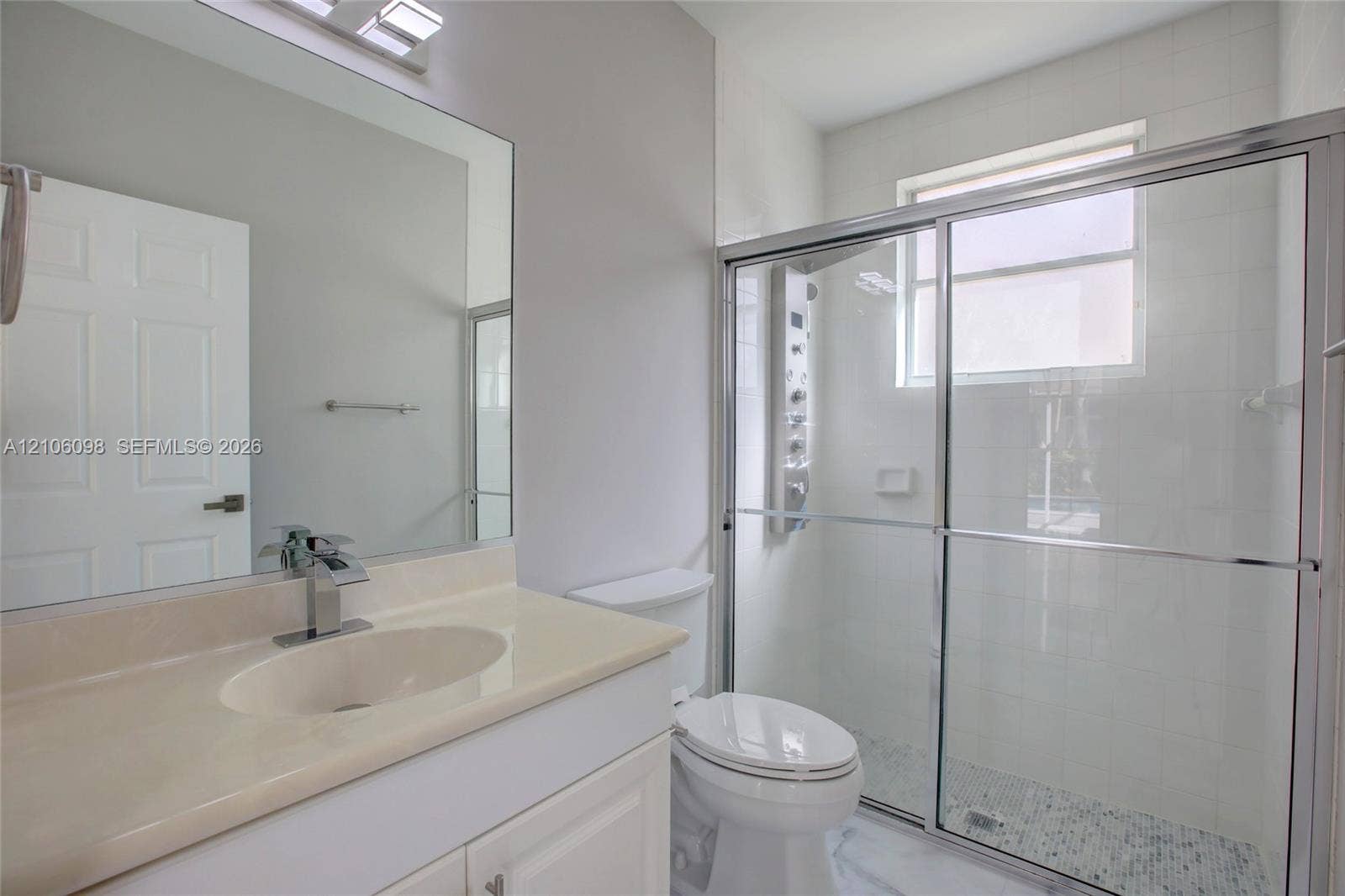 Bathroom featuring a vanity with integrated sink, large wall-mounted mirror, walk-in shower with a glass enclosure, rainfall shower panel system, and tile flooring