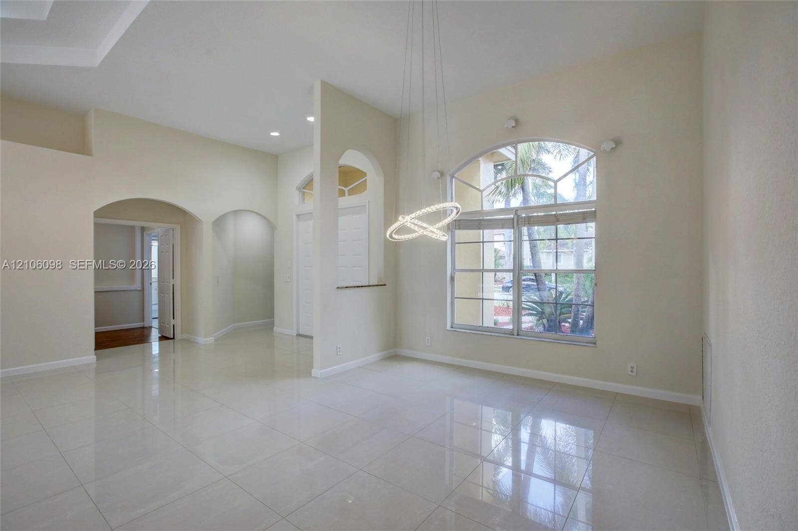 Open-concept interior featuring polished tile flooring, arched wall cutouts, a contemporary circular pendant light fixture, and a large arched multi-pane window