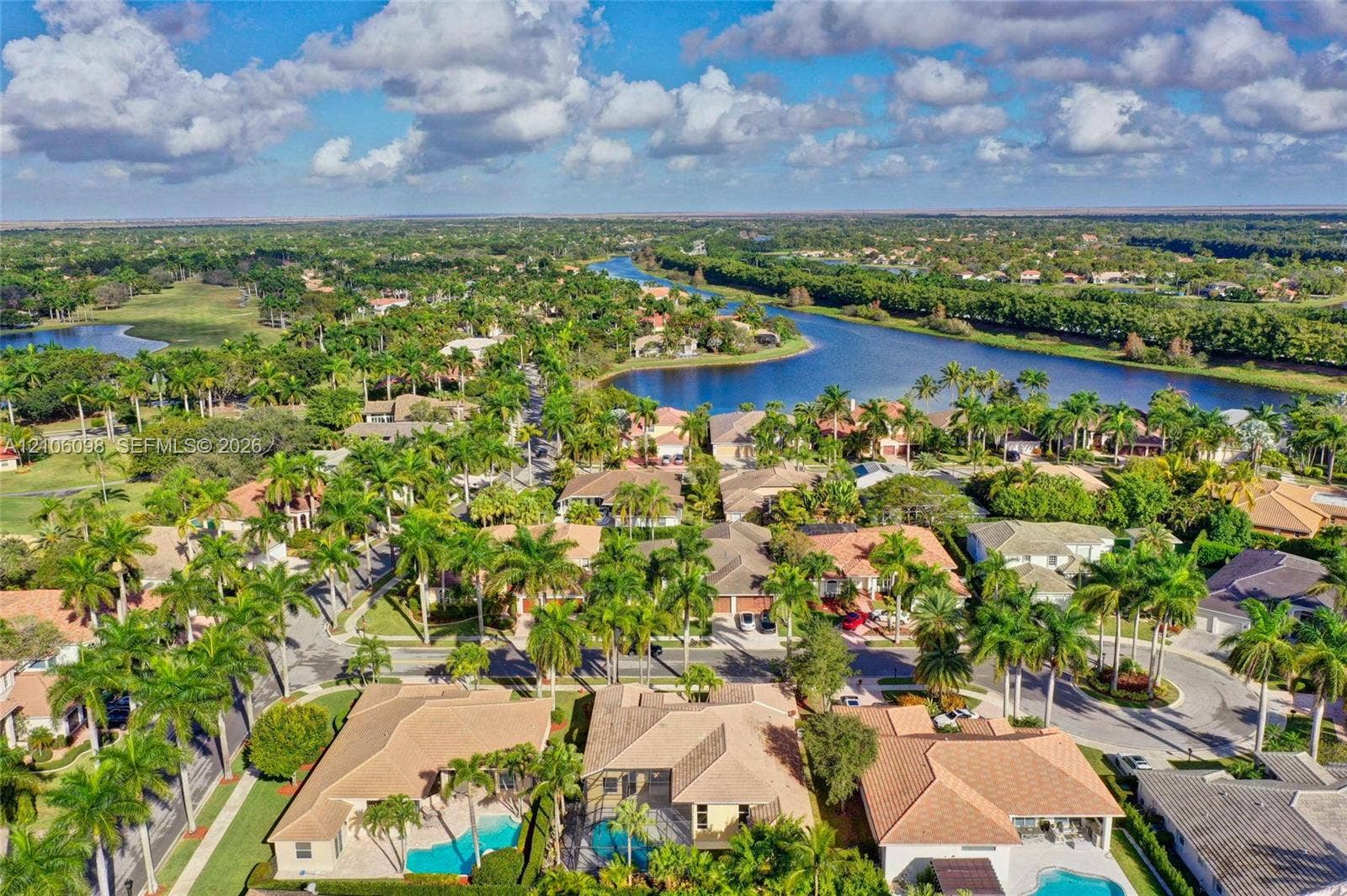 Aerial perspective featuring residential lots with private swimming pools, tile roofing, and mature tropical landscaping within a waterfront community