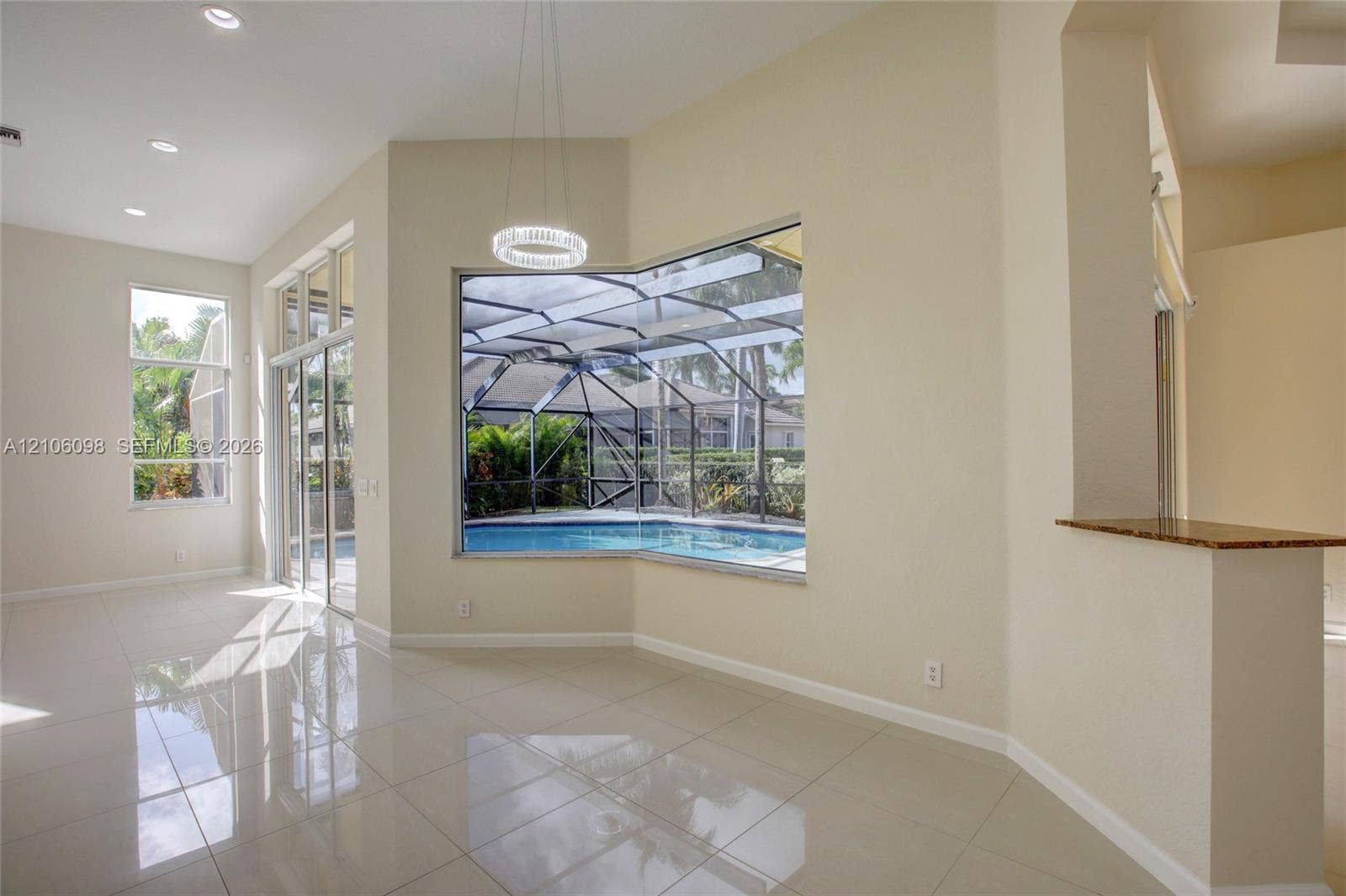 Open-concept interior featuring polished tile flooring, recessed lighting, a built-in stone-surface counter, and large windows encompassing a screened-in pool enclosure