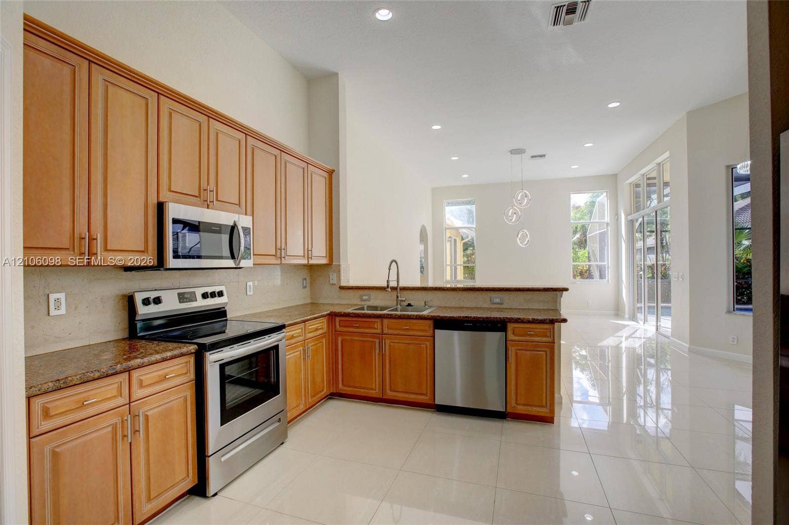 Kitchen featuring natural wood cabinetry, stone countertops, stainless steel appliances, recessed lighting, and large-format tile flooring