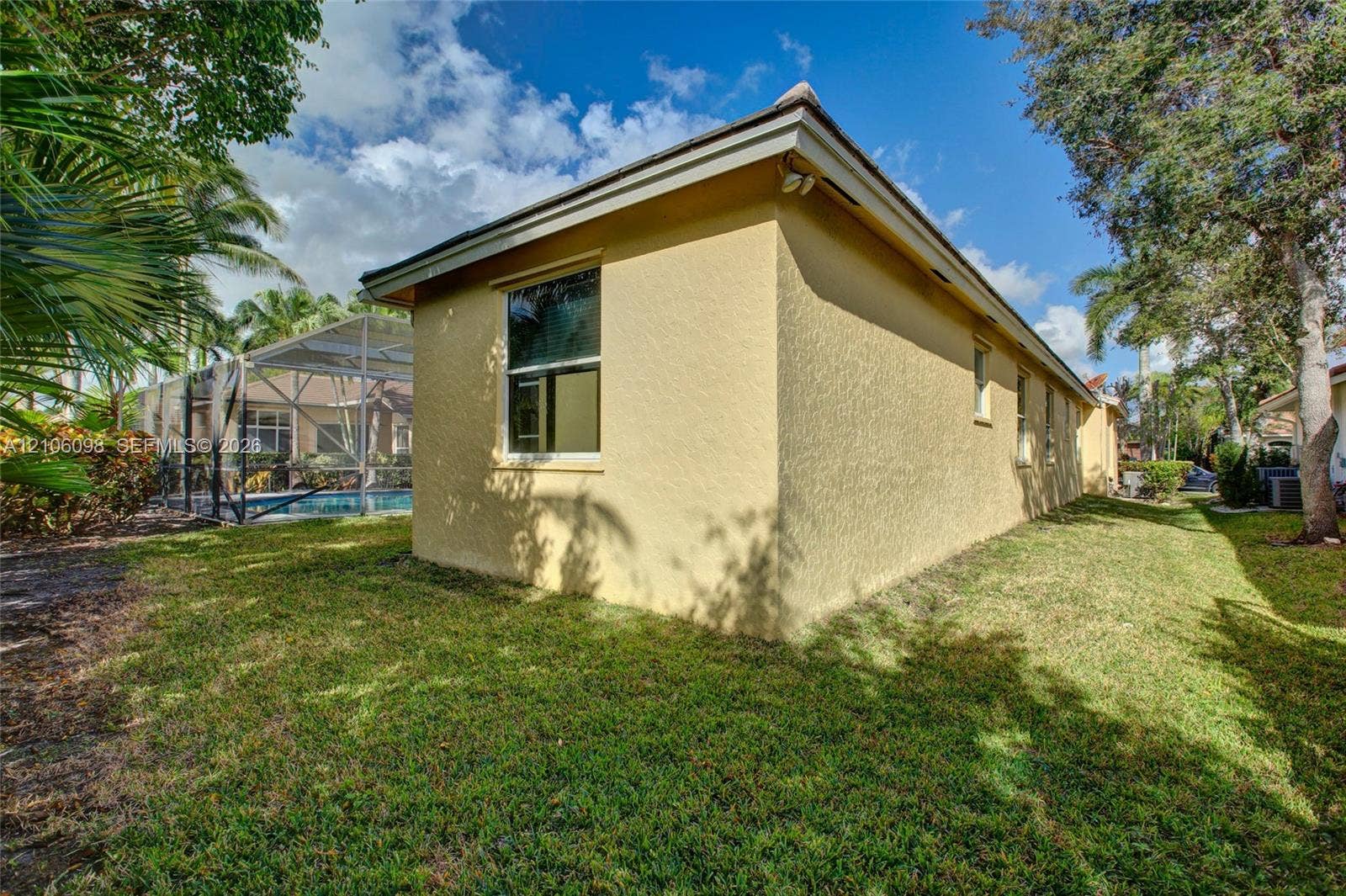 Stucco exterior, screened-in swimming pool enclosure, and mature landscaping