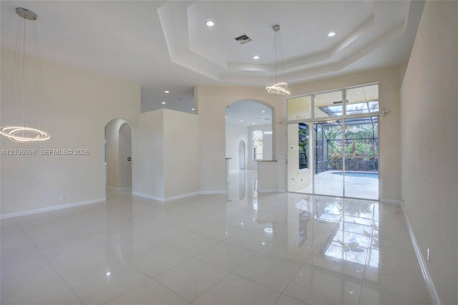 Open interior featuring a tray ceiling, recessed lighting, modern geometric pendant light fixtures, light-toned tile flooring, and floor-to-ceiling glass sliding doors