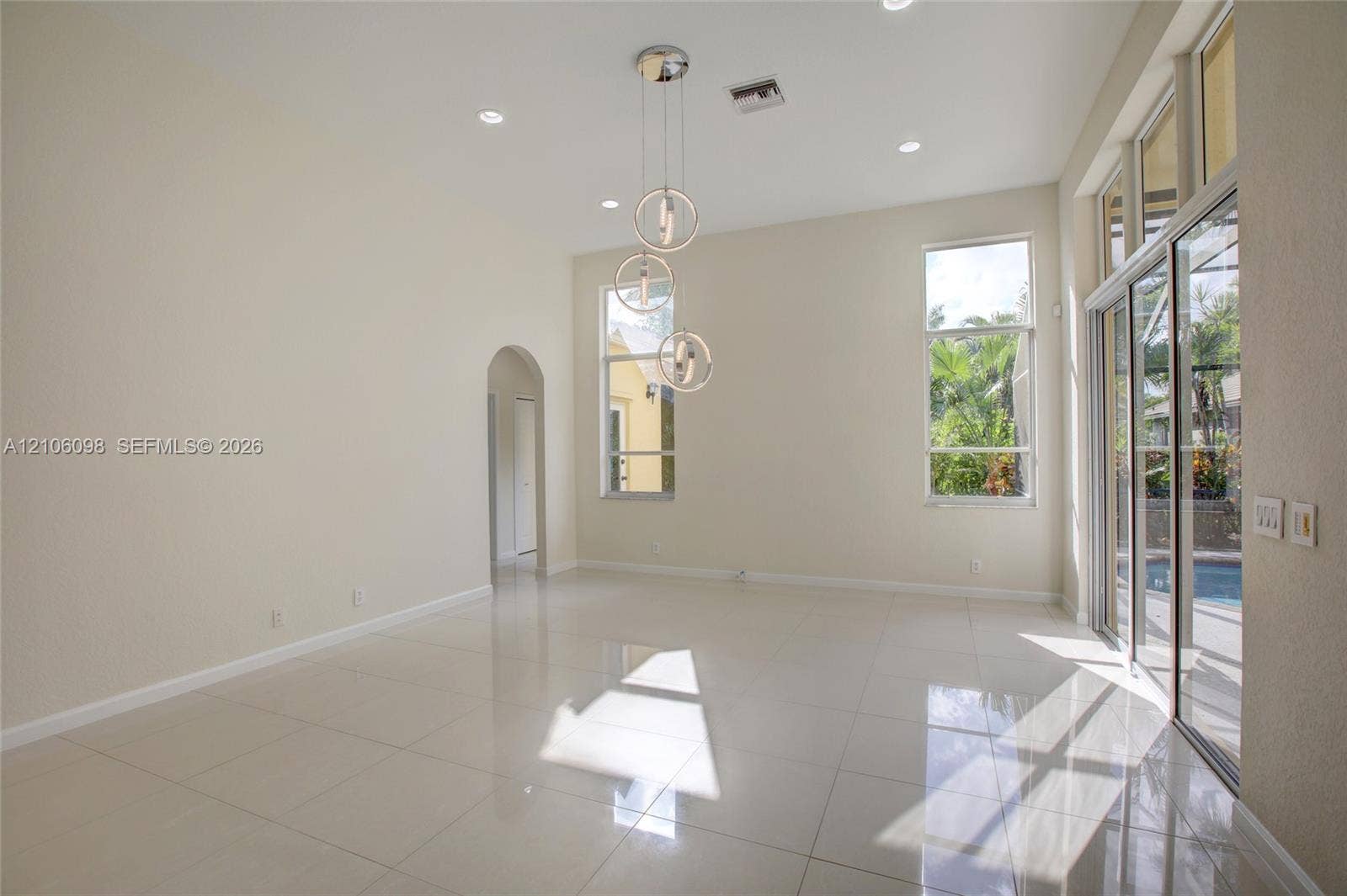 High-ceiling living area featuring large-format tile flooring, a multi-tier contemporary pendant light fixture, arched entryways, and sliding glass doors