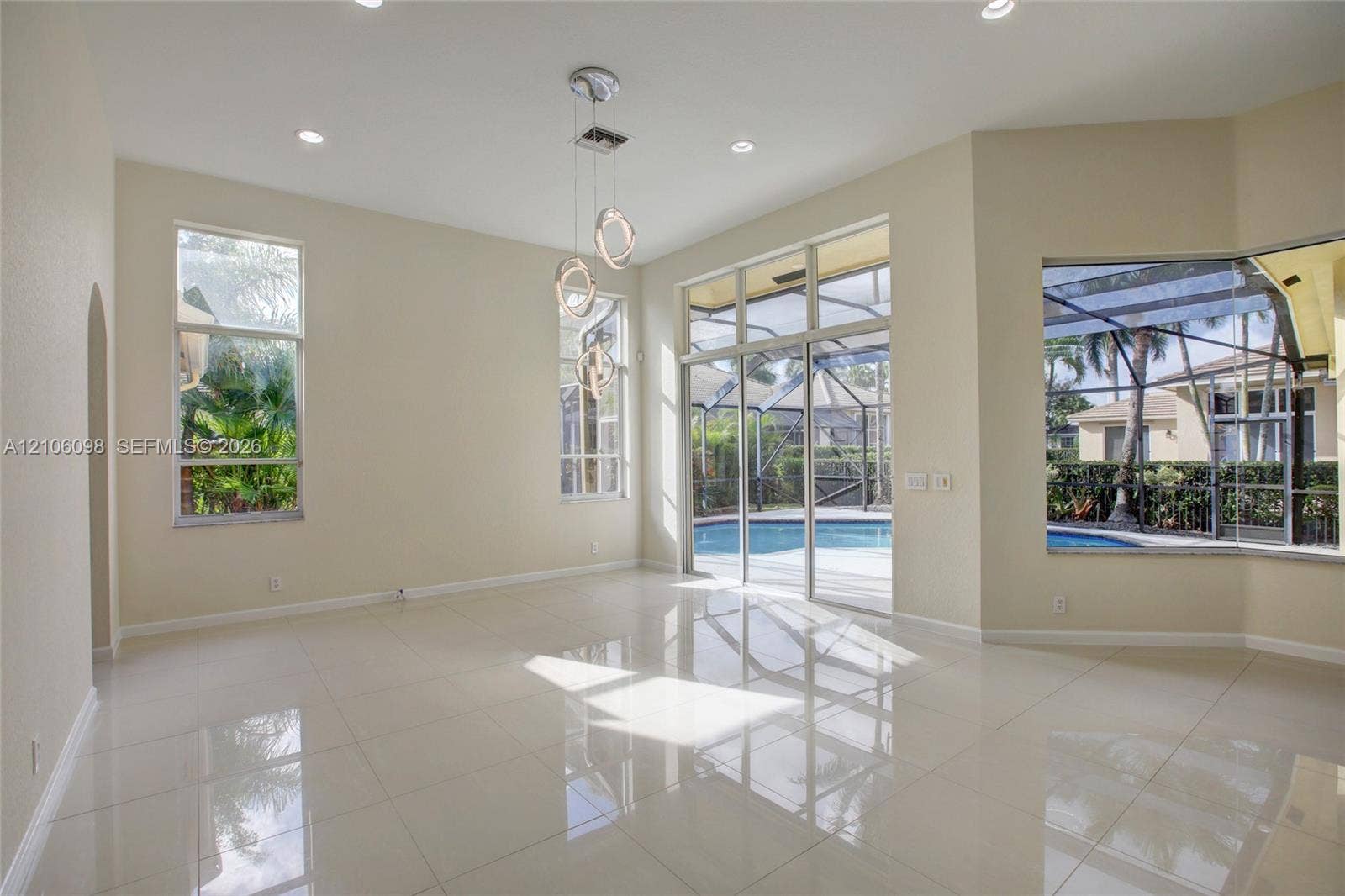 High ceilings with recessed lighting, large-format tile flooring, multi-light pendant fixture, floor-to-ceiling windows, and sliding glass doors opening to a screened-in pool enclosure
