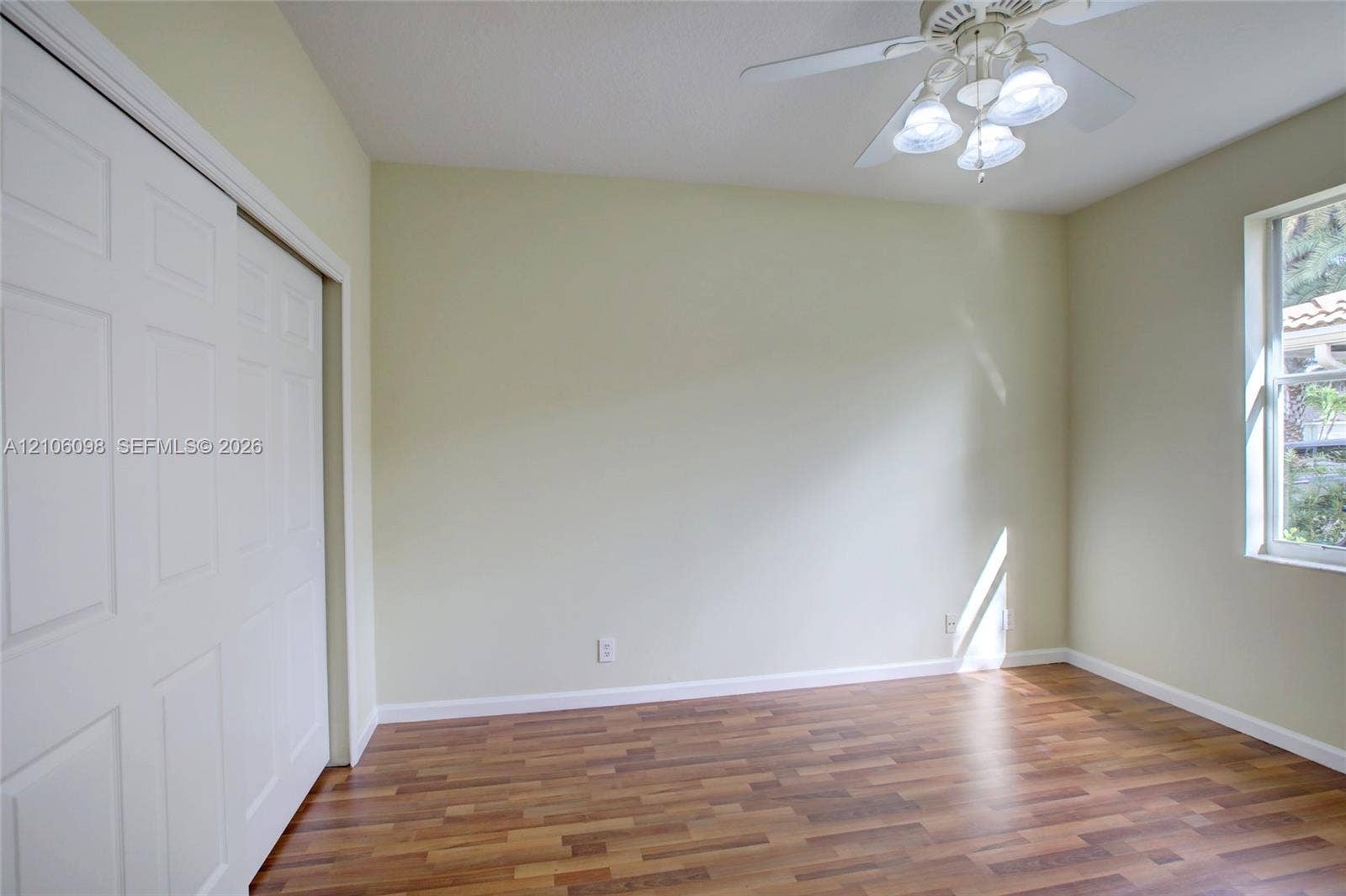 Wood-finish flooring, white sliding closet doors, and a ceiling fan with integrated lighting
