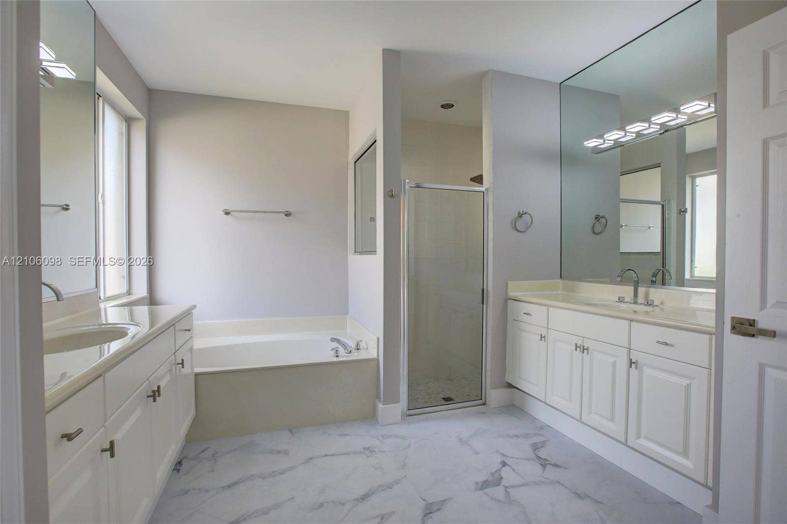 Bathroom featuring dual white vanities with surface-mounted sinks, a built-in soaking tub, a glass-enclosed shower, and large-format flooring