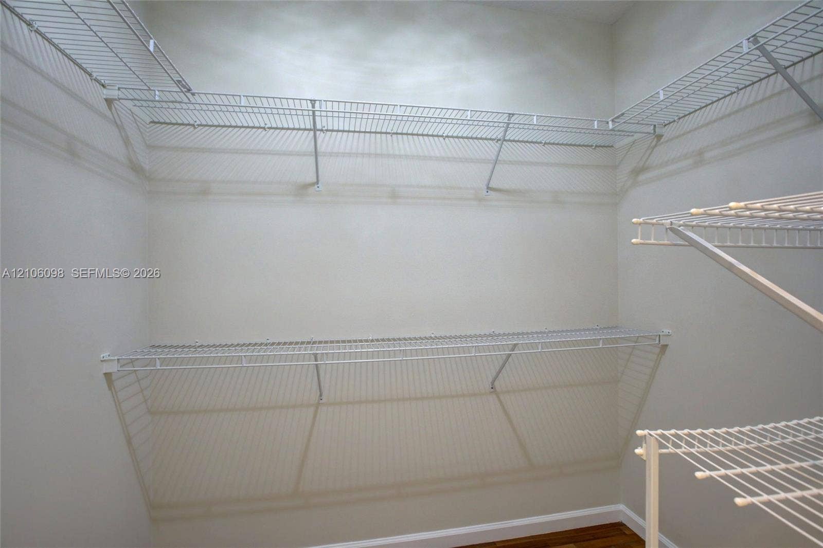 Walk-in storage space featuring multi-tiered white wire shelving and wood-finish flooring