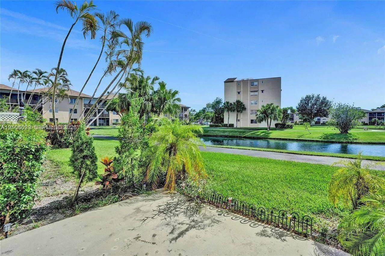 7840 NW 50th Street, #105, Lauderhill, FL 33351 Concrete patio featuring low-profile decorative metal fencing, manicured lawn, established palm trees, and a waterway