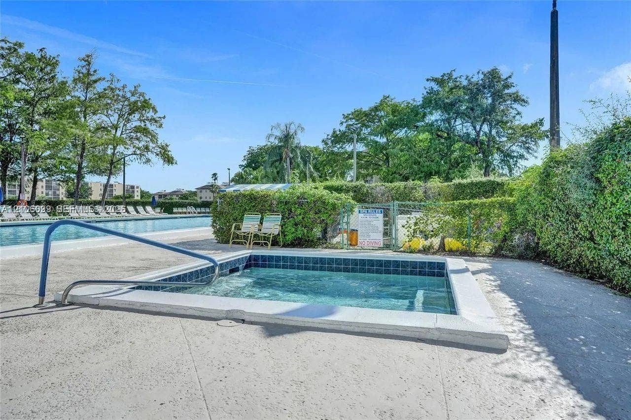 7840 NW 50th Street, #105, Lauderhill, FL 33351 In-ground spa featuring blue tile trim and a metal handrail, situated on a concrete pool deck with manicured perimeter landscaping