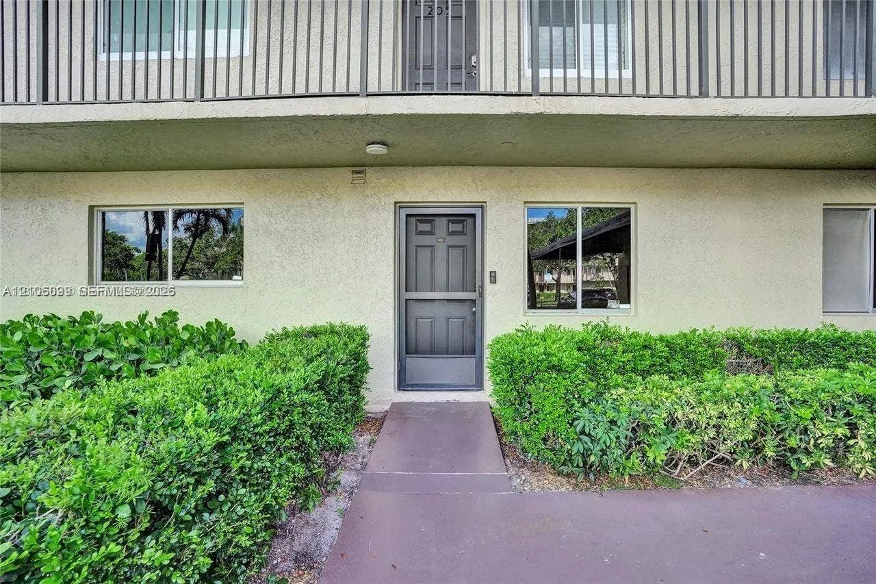 7840 NW 50th Street, #105, Lauderhill, FL 33351 Stucco exterior featuring an entry door with a screen door, windows with aluminum frames, and a concrete walkway bordered by established shrubbery