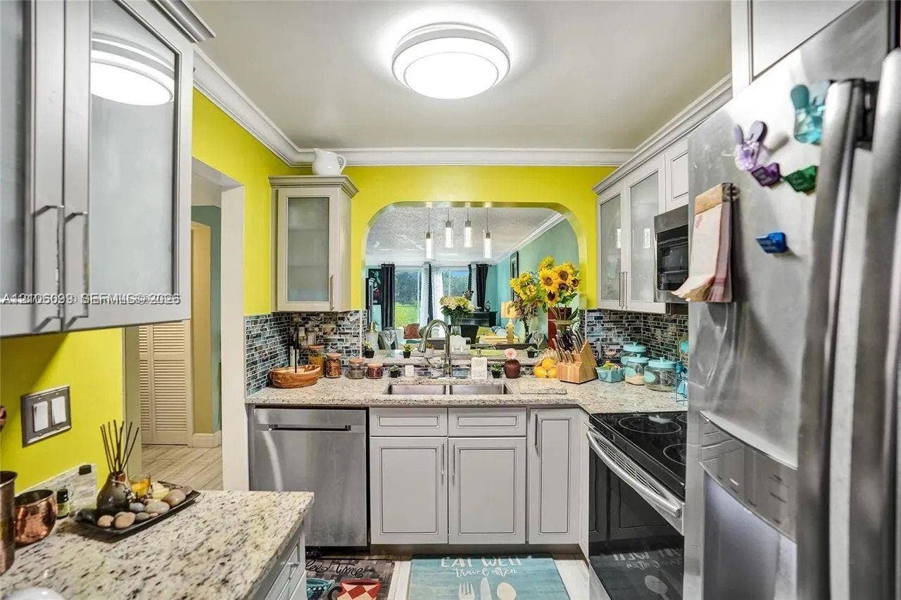 7840 NW 50th Street, #105, Lauderhill, FL 33351 Kitchen featuring light-gray cabinetry, stone-finish countertops, stainless steel appliances, decorative tile backsplash, and a pass-through window with an arched header