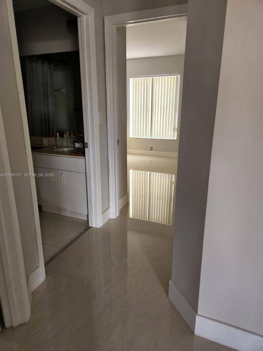 16284 SW 100th Terrace, Miami, FL 33196 Interior hallway featuring large-format tile flooring, white shaker-style vanity cabinetry with a solid surface countertop, and vertical blind window treatments