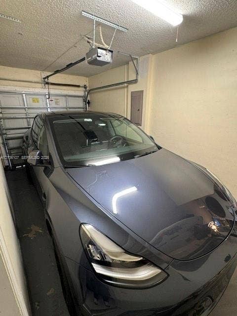 16284 SW 100th Terrace, Miami, FL 33196 Enclosed garage featuring an automated overhead door opener, linear lighting fixture, and electrical service panel