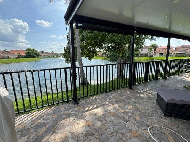16284 SW 100th Terrace, Miami, FL 33196 Covered patio featuring a flagstone-patterned paved floor and black metal railings, overlooking a lake with mature landscaping