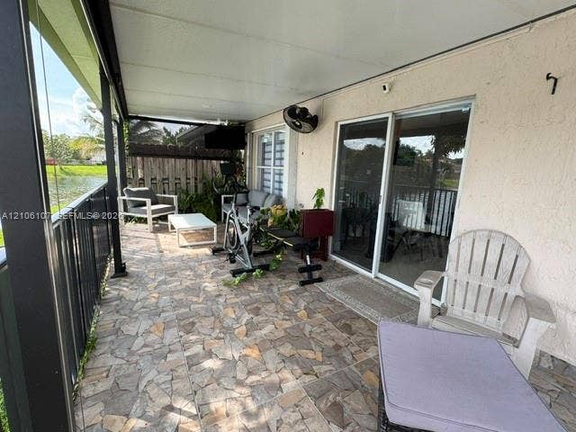 16284 SW 100th Terrace, Miami, FL 33196 Covered patio featuring stone-tiled flooring, black metal railing, sliding glass doors, and a mounted wall fan