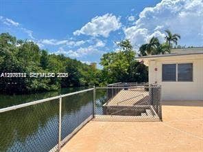 Waterfront patio featuring a concrete deck, chain-link fencing, and mature perimeter trees