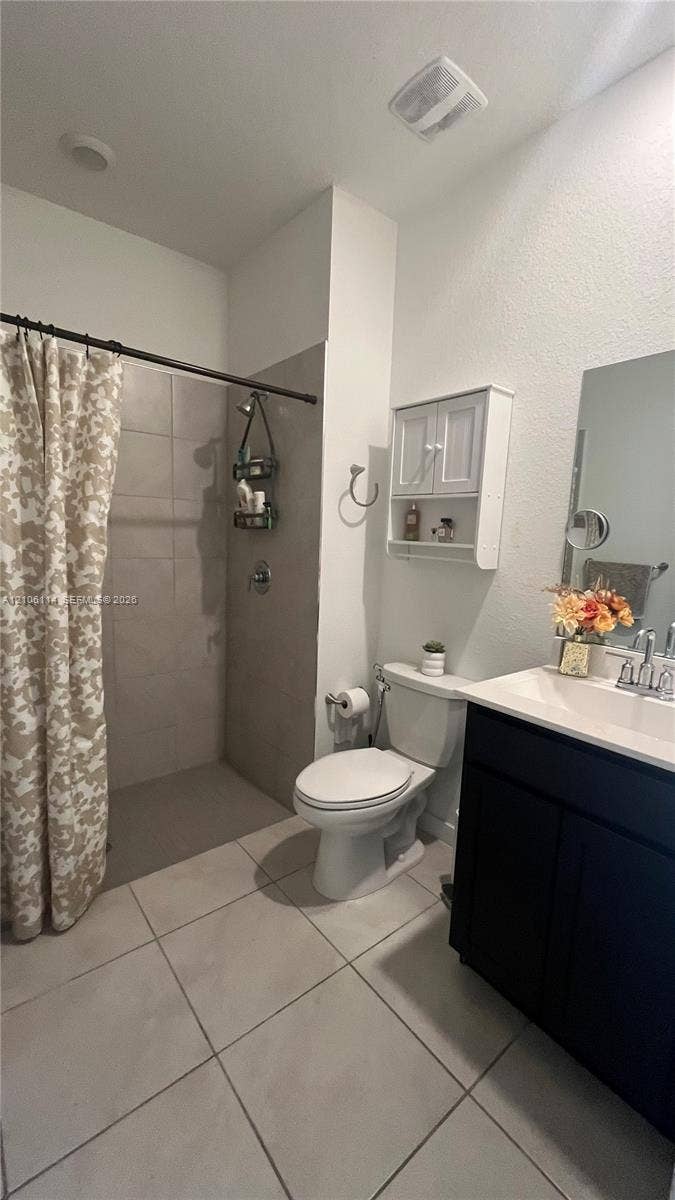 Bathroom featuring large-format tile flooring, dark cabinetry with a white countertop, walk-in shower with full-height neutral wall tile, and built-in wall cabinetry