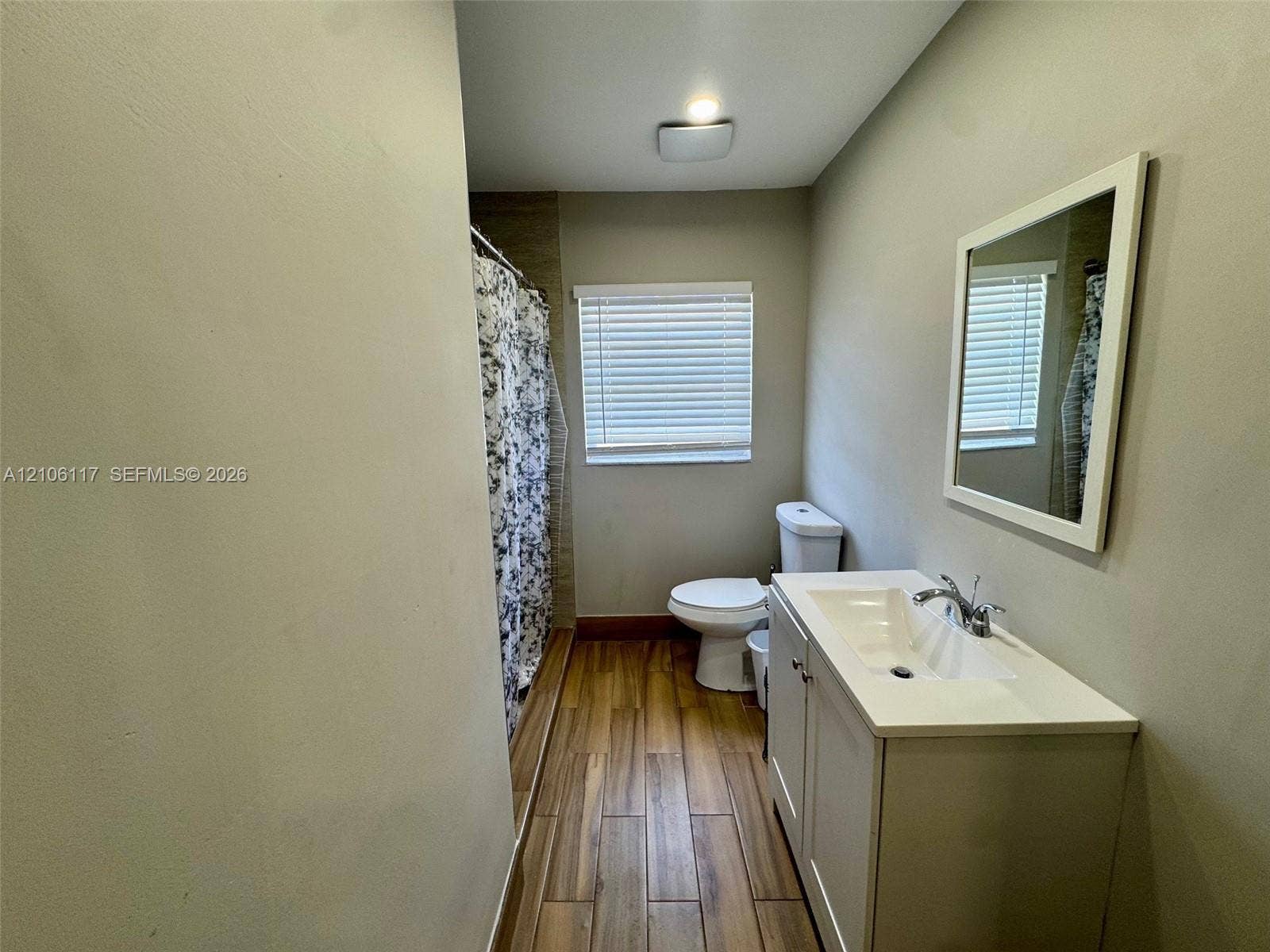 Bathroom featuring wood-finish flooring, a vanity with a rectangular sink, wall-mounted mirror, and horizontal window blinds