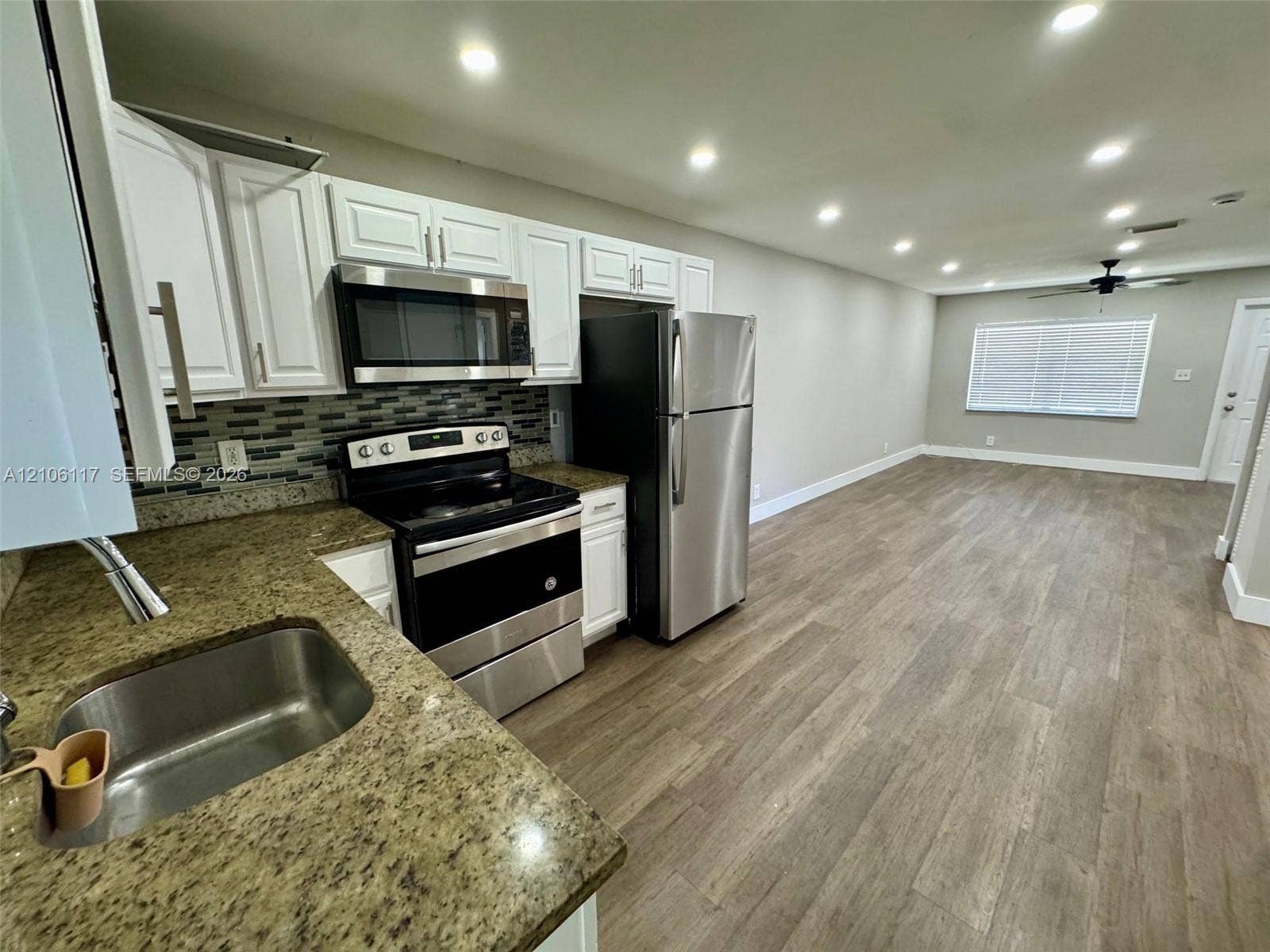 Kitchen featuring white shaker-style cabinetry, stone countertops, stainless steel appliances, a tile backsplash, and wood-finish flooring
