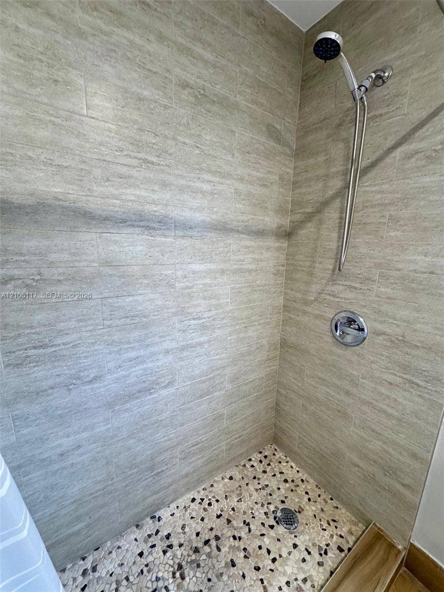 Shower featuring horizontal stone-textured wall tile, pebble-mosaic flooring, and a chrome hand-held showerhead with integrated wall-mounted pressure control