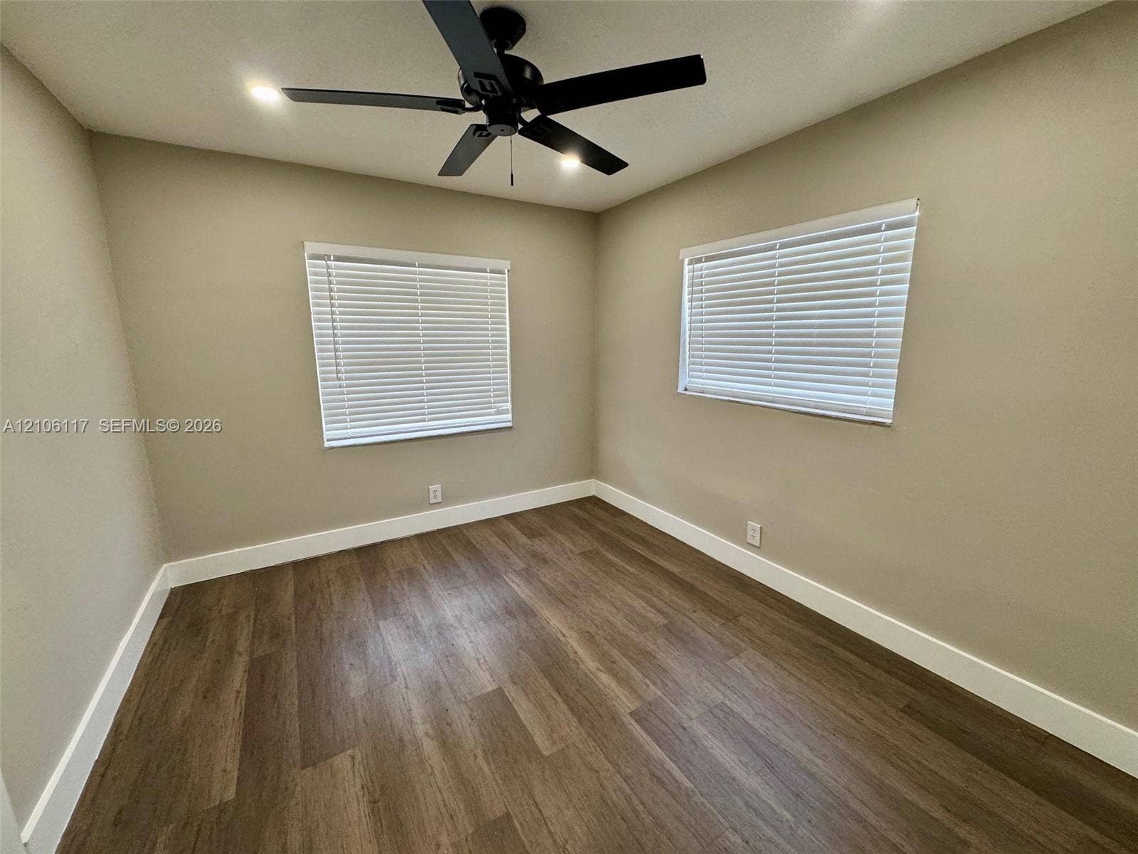Neutral wall finishes, wood-finish flooring, two windows with horizontal blinds, and a ceiling fan with integrated lighting