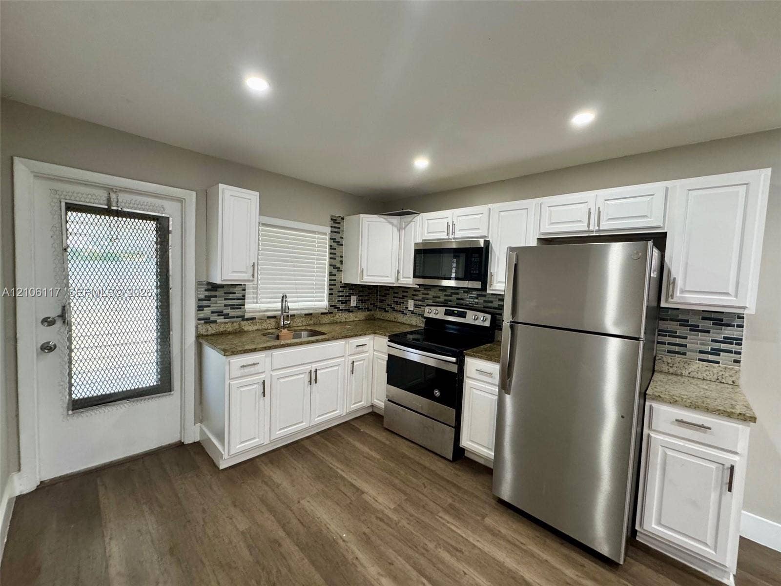 Kitchen featuring white cabinetry, stone-surface countertops, multi-toned mosaic tile backsplash, stainless steel appliances, and wood-finish flooring