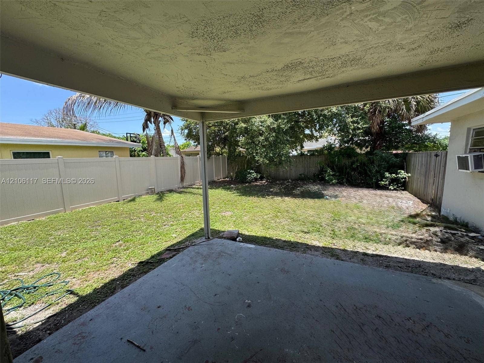 Covered concrete patio overlooking a private backyard enclosed by vinyl fencing with mature landscaping