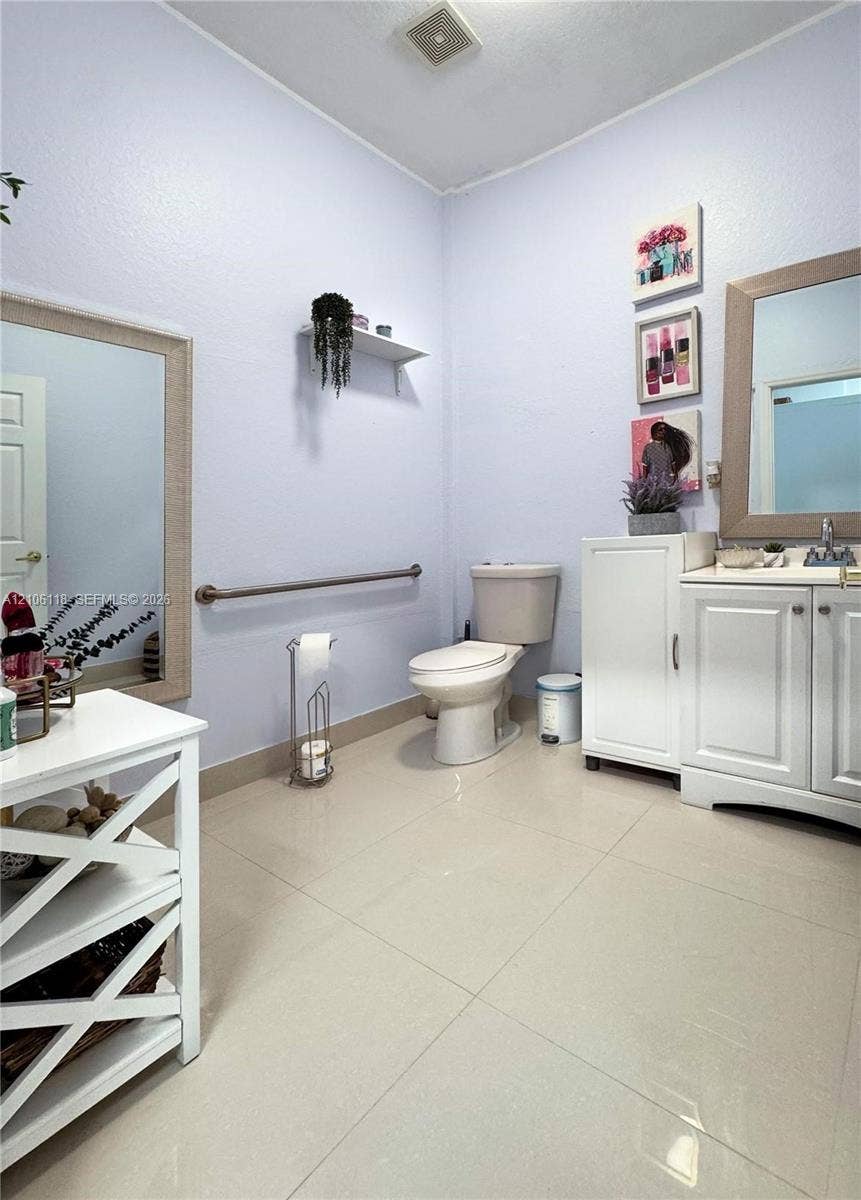 Bathroom featuring large-format tile flooring, a white vanity with integrated cabinetry, and a wall-mounted metal support bar