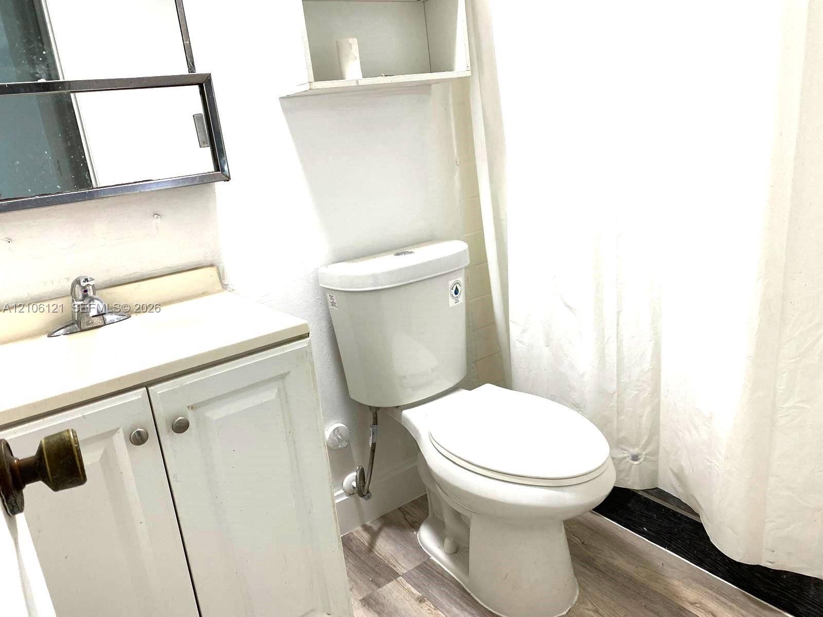 Bathroom featuring white cabinetry, integrated sink, wall-mounted medicine cabinet, built-in recessed wall shelving, and wood-finish flooring