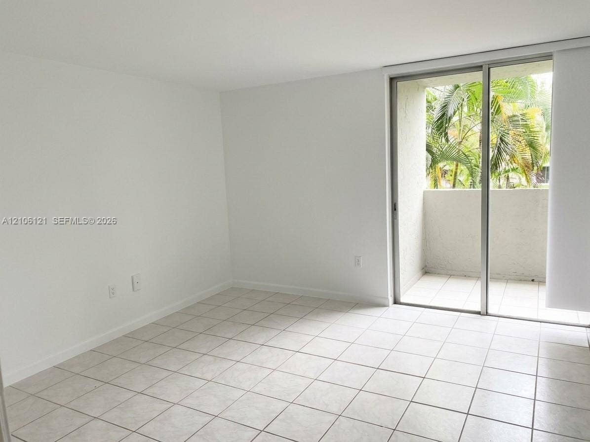 Neutral-toned tile flooring, white walls, and a sliding glass door providing access to a private balcony