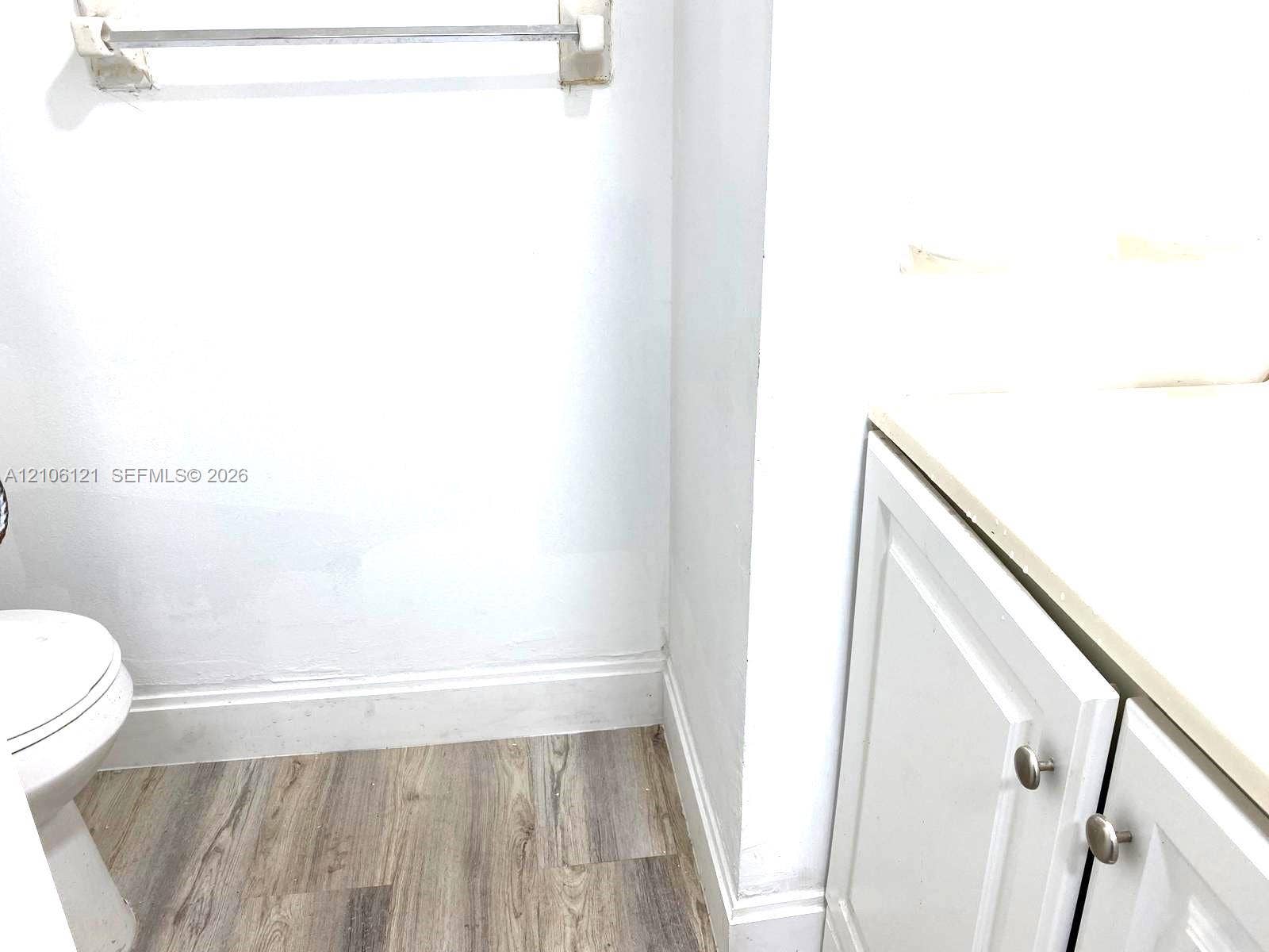 Bathroom featuring wood-finish flooring, white cabinetry with round metallic hardware, and a solid-surface countertop